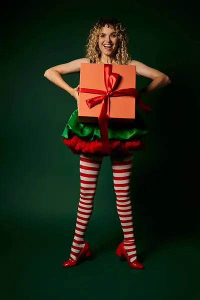 Cheerful blonde woman in new year elf costume holding gift in front of her and smiling at camera — Stock Photo