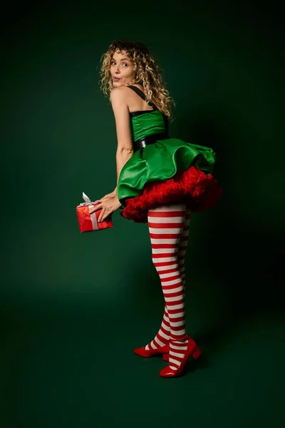Jolly woman in new year elf costume posing with pouted lips and holding huge present in hands — Stock Photo