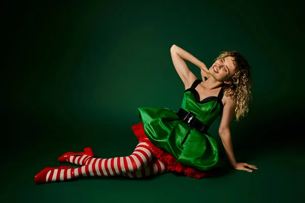 Attrayant femme habillée comme nouvel an elfe légèrement inclinable sur le sol posant sur fond vert — Photo de stock
