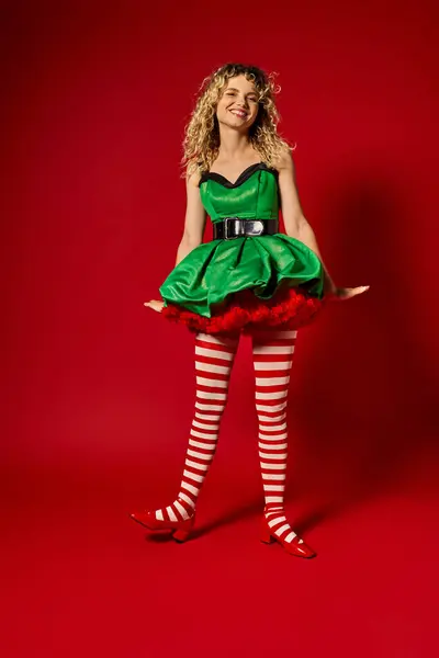 Gaie blonde nouvel an elfe debout toujours en robe verte festive et bas souriant à la caméra — Photo de stock