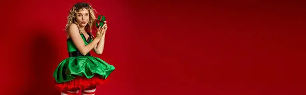 Дивовижний новорічний ельф в зеленій сукні з розтертими губами, тримаючи подарунок і дивлячись на камеру, банер — стокове фото