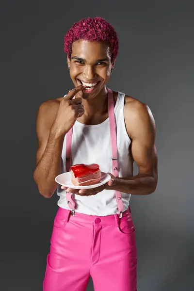 Alegre afroamericano hombre sosteniendo corazón en forma de mini pastel y mirando a la cámara, la moda y el estilo - foto de stock