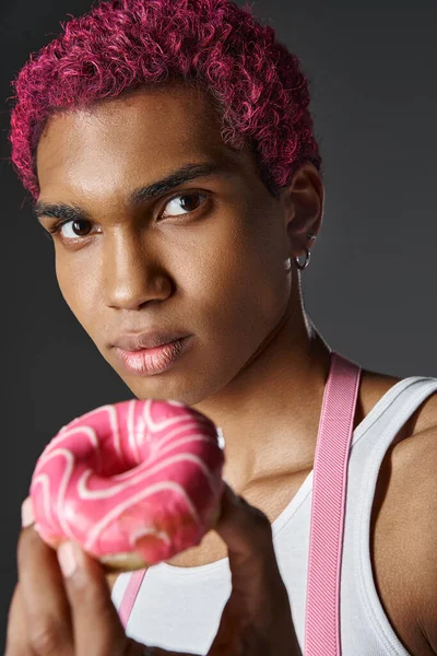Retrato de un joven afroamericano con pelo rosa posando con rosquilla, moda y estilo - foto de stock