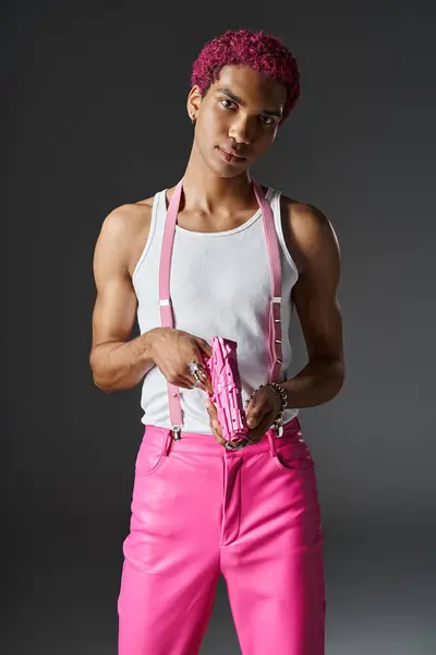 Bonito rosa cabelos modelo masculino com acessórios de prata e suspensórios rosa segurando arma de brinquedo rosa — Fotografia de Stock
