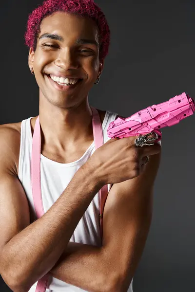 Портрет веселого молодого чоловіка з рожевим волоссям і підтяжки позує іграшковий пістолет і щасливо посміхається — стокове фото