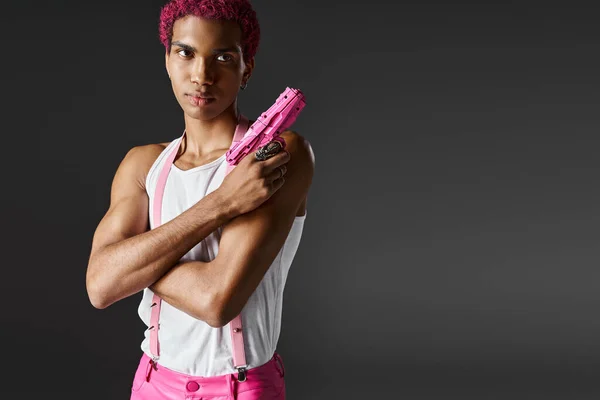 Modisch gut aussehendes männliches Model mit rosa Haaren posiert mit Spielzeugpistole und schaut ernst in die Kamera — Stockfoto
