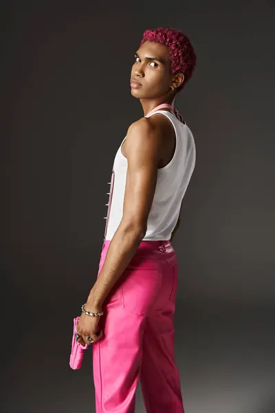 Serious african american male model in vibrant pink attire posing with toy gun on gray backdrop — Stock Photo