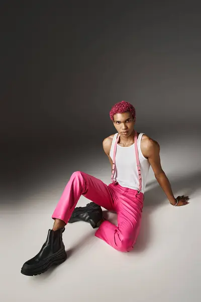 Homem de cabelos rosa elegante em roupa vibrante rosa com botas pretas sentado no chão, conceito de moda — Fotografia de Stock