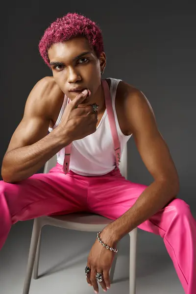 Stylish young man sitting on white chair with hand under his chin looking at camera, fashion concept — Stock Photo