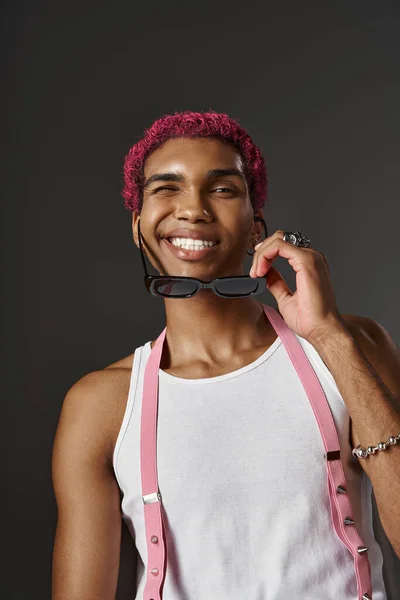 Homem elegante alegre com suspensórios tirando seus óculos de sol e sorrindo feliz, conceito de moda — Fotografia de Stock