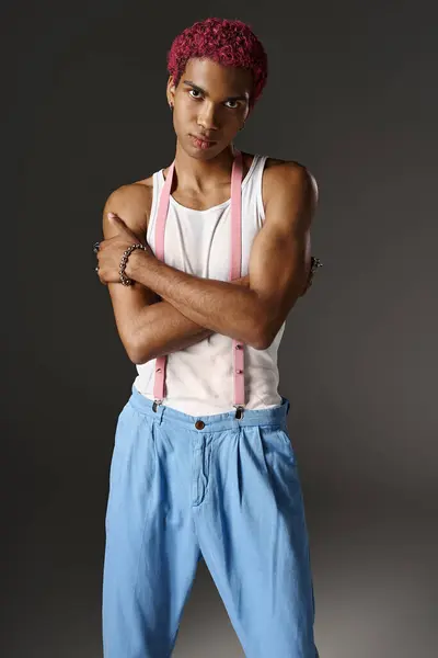 Handsome man in blue pants with pink suspenders posing with slightly crossed arms, fashion concept — Stock Photo