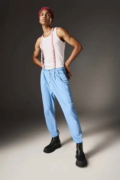 Молодой модный мужчина в синих штанах с подтяжками, позирующий руками за спиной, концепция моды — стоковое фото