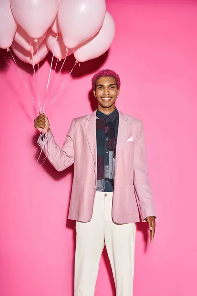 Gai mâle modèle souriant heureux avec des ballons dans les mains et en regardant la caméra sur fond rose — Photo de stock