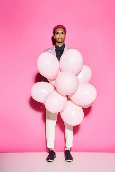 Bel homme aux cheveux roses tenant des ballons roses et regardant la caméra posant sur fond rose — Photo de stock