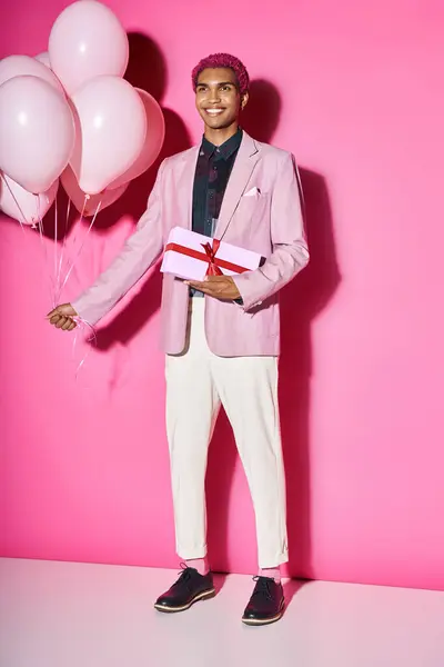 Handsome african american male model posing unnaturally with balloons and present in hands — Stock Photo