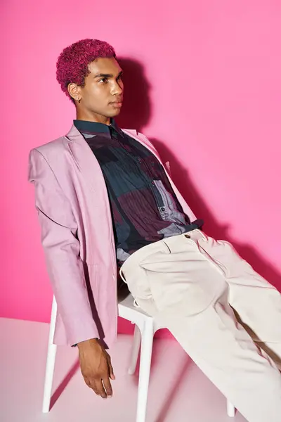 Handsome african american man acting like male doll in pink blazer and sitting on white chair — Stock Photo