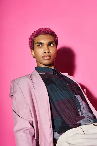 Красивый мужчина с вьющимися розовыми волосами позирует на розовом фоне и смотрит в сторону на розовый фон — стоковое фото