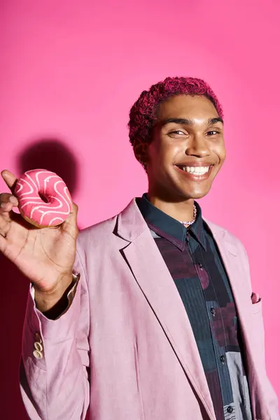 Joyeux jeune homme souriant anormalement et montrant beignet à la caméra posant sur fond rose — Photo de stock