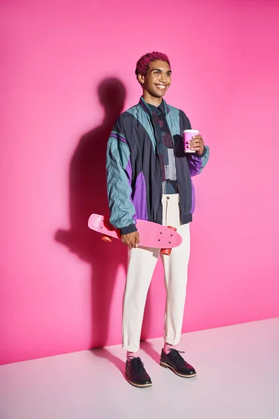 Весела стильна чоловіча модель позує з чашкою кавового паперу та скейтбордом, діючи як чоловіча лялька — стокове фото