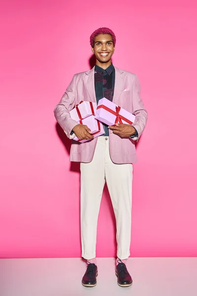 Cheerful young man posing unnaturally with presents in his hands posing on pink background — Stock Photo