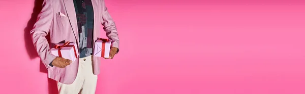 Vue recadrée du jeune homme élégant en tenue vibrante avec des cadeaux dans les mains sur fond rose, bannière — Photo de stock