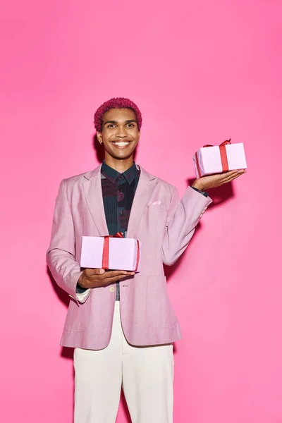 Весела молода чоловіча модель позує з подарунками в руках на рожевому тлі, діючи як лялька — стокове фото