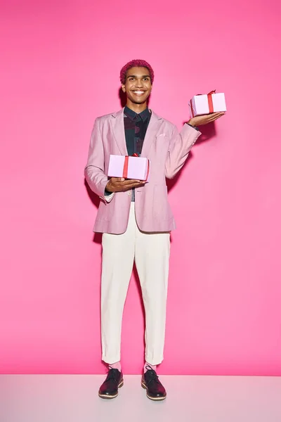 Handsome african american man in vibrant outfit posing with presents in hands on pink backdrop — Stock Photo