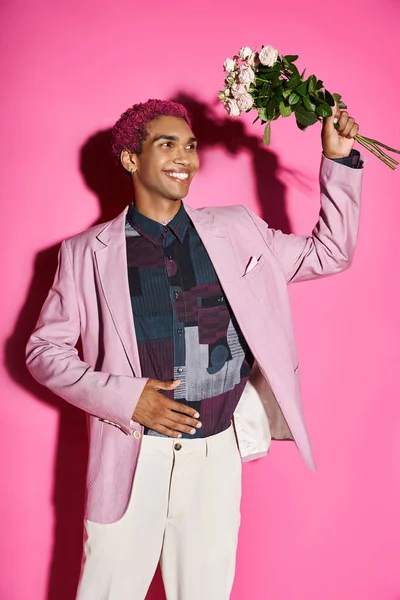 Cheerful young man in pink blazer posing like doll with rose bouquet in hands and looking away — Stock Photo
