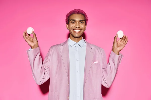 Handsome young male model smiling unnaturally and holding delicious zefir in hands on pink backdrop — Stock Photo