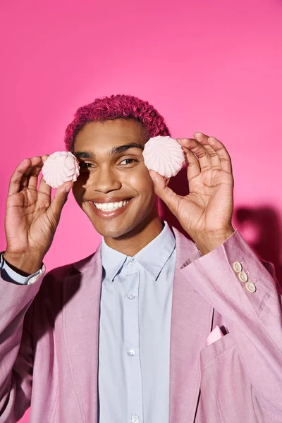 Homem alegre posando com delicioso zefir rosa perto do rosto e olhando para a câmera no fundo rosa — Fotografia de Stock