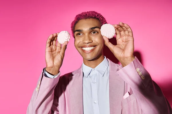 Hombre alegre posando con delicioso zefir rosa cerca de la cara sobre fondo rosa, actuando como muñeca masculina - foto de stock
