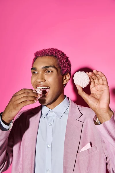Jovem alegre agindo de forma não natural enquanto come delicioso zefir rosa posando em pano de fundo rosa — Fotografia de Stock