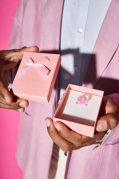 Vista ritagliata di giovane uomo afroamericano che tiene piccolo regalo rosa con anello a forma di cuore — Foto stock