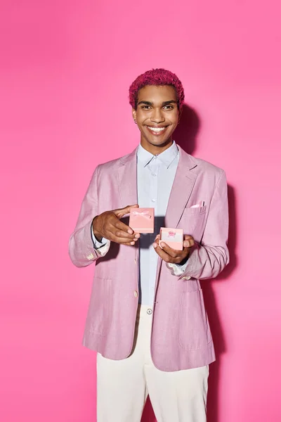 Cheerful young man posing unnaturally with present in his hands smiling at camera on pink backdrop — Stock Photo
