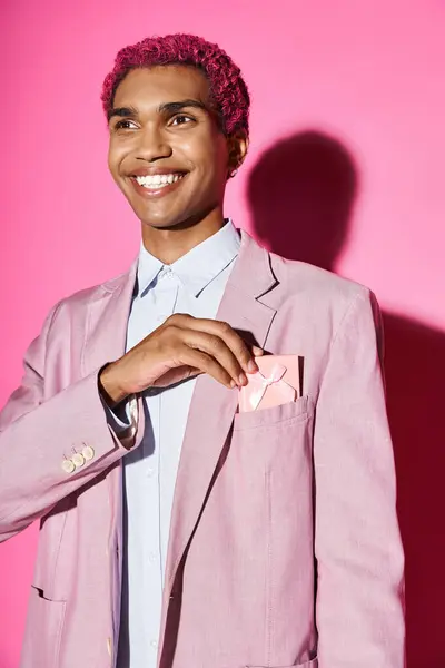 Jovem rosa de cabelos modelo masculino em roupas vibrantes sorrindo de forma não natural com presente em seu bolso — Fotografia de Stock