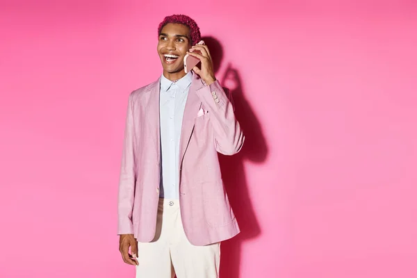 Young stylish man acting unnaturally smiling cheerfully and talking by phone on pink background — Stock Photo