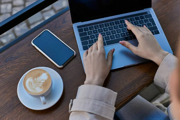 Vue du dessus de la femme tapant sur ordinateur portable tout en travaillant à distance près de tasse de café et smartphone dans le café — Photo de stock