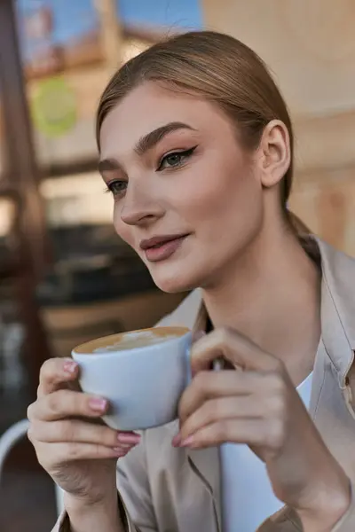 Elegante donna bionda in trench godendo la sua tazza di cappuccino in caffè, atmosfera rilassata — Foto stock
