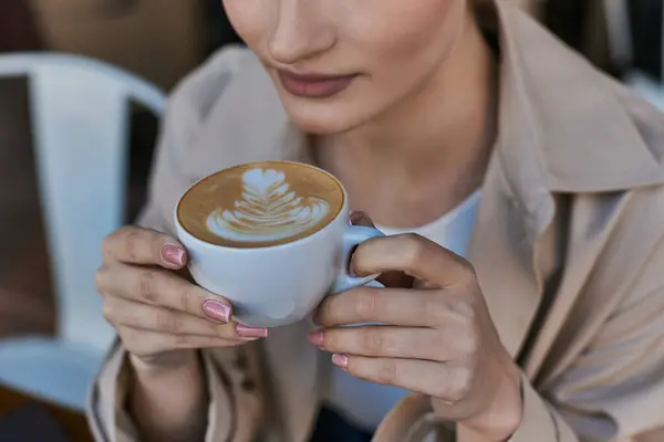 Vista cortada da mulher em casaco de trincheira desfrutando de sua xícara de cappuccino no café, atmosfera relaxada — Fotografia de Stock
