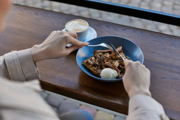 Vue recadrée de la femme mangeant ses gaufres belges avec une cuillère à crème glacée sur l'assiette à côté de la tasse de café — Photo de stock