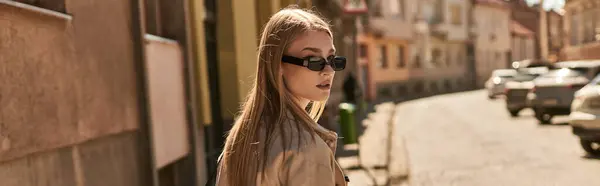 Junge blonde Frau in schickem Trenchcoat und Sonnenbrille, die an sonnigen Tagen auf der Straße spaziert, Banner — Stockfoto
