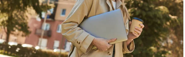 Banner of cropped woman in trench coat walking with laptop and takeaway coffee, freelancer in city — Stock Photo