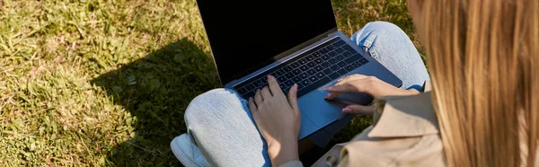 Overhead view, woman in jeans and trench coat sitting on green lawn and using laptop, banner — Stock Photo