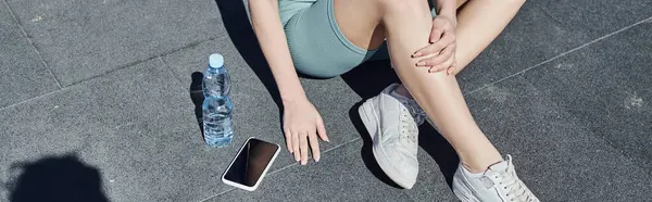 Abgeschnittenes Banner einer Sportlerin in Activwear, die neben Wasserflasche und Smartphone auf dem Boden sitzt — Stockfoto