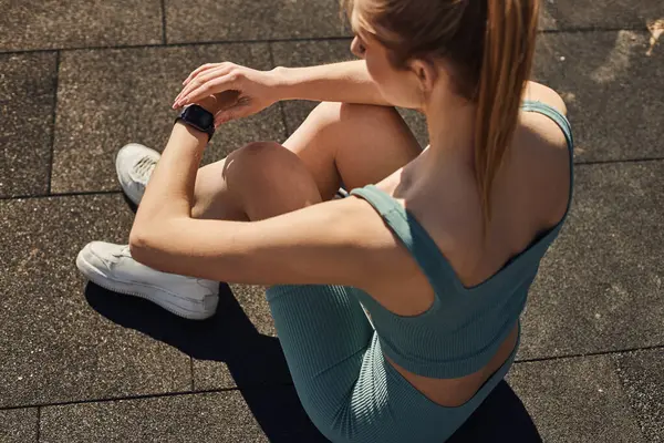 Vista superior de la joven deportista en ropa deportiva sentada y comprobando el rastreador de fitness después del entrenamiento - foto de stock
