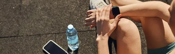 Банер спортсменки в активному одязі перевіряє фітнес-трекер поруч зі смартфоном і пляшкою води — стокове фото