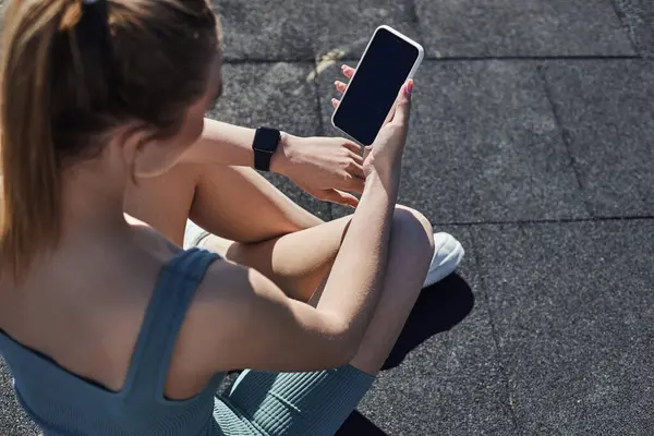 Top view of fit woman in activewear with fitness tracker on wrist using smartphone after workout — Stock Photo