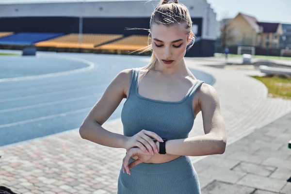Jovem mulher em activewear apertado verificando rastreador de fitness no pulso após o treino, fitness e saúde — Fotografia de Stock
