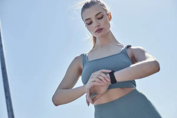 Low angle view of young woman in activewear checking fitness tracker on wrist after workout — Stock Photo