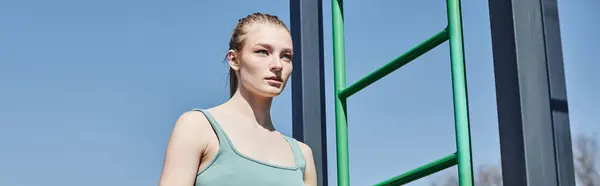 Banner of young blonde woman in crop top standing near vertical ladder outside in sunny day — Stock Photo